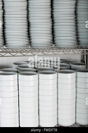 Pile di molte piastre bianche su un filo il ripiano di un rack in una cucina commerciale Foto Stock