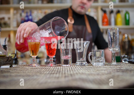 Il barista versa vari di bere alcol in piccoli bicchieri in bar Foto Stock