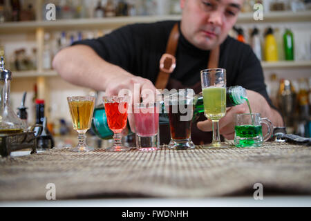 Il barista versa vari di bere alcol in piccoli bicchieri in bar Foto Stock