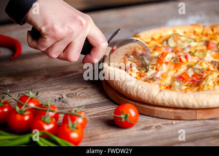 Affettare la pizza fresca con rullo coltello. Foto Stock