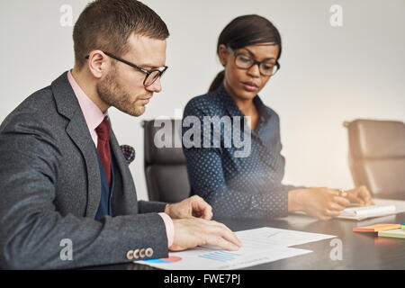 Imprenditore e donna avente una riunione seria seduti insieme la lettura di un documento o una relazione con la messa a fuoco di un giovane uomo nella glasse Foto Stock