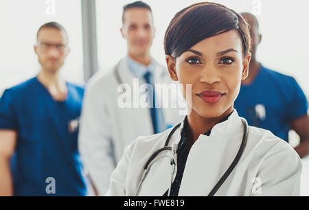 Medico donna davanti al team, uno stetoscopio attorno al collo guardando fiduciosi Foto Stock