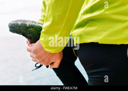 Primo piano di un giovane sportivo caucasica indossando indumenti sportivi il suo stiramento del quadricipite prima o dopo l'esecuzione Foto Stock
