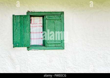 Aperto a metà vecchia finestra con persiane di legno e un bianco fatti a mano e tendaggi rossi. Foto Stock