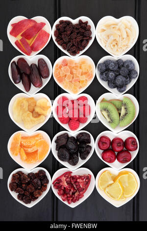 Secca e fresca frutta mista super selezione di cibo in forma di cuore ciotole di legno su sfondo nero. Foto Stock