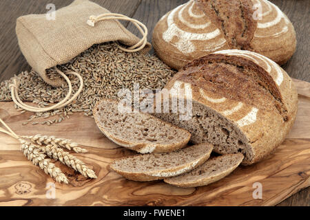 Freschi di forno in casa pane di segale su un olive wood board con guaine di frumento e di grano in un sacco di Hesse su sfondo di quercia. Foto Stock