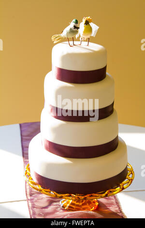 Un bianco tradizionale torta di nozze è condito con uccelli di artigianato e avvolto in nastro viola a la sposa e lo sposo della reception. Foto Stock