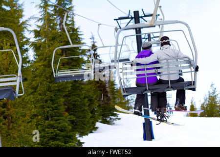 Un paio di persone ride sci seggiovia fino alla montagna insieme mentre è seduto vicino a ogni altro avente un momento divertente durante Foto Stock