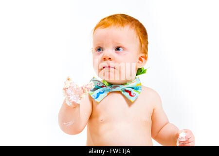 Un bambino arriva a mangiare la torta per la prima volta il suo primo compleanno in questa torta smash in studio contro uno sfondo bianco. Foto Stock