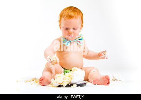 Un bambino arriva a mangiare la torta per la prima volta il suo primo compleanno in questa torta smash in studio contro uno sfondo bianco. Foto Stock