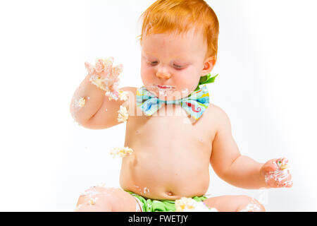 Un bambino arriva a mangiare la torta per la prima volta il suo primo compleanno in questa torta smash in studio contro uno sfondo bianco. Foto Stock