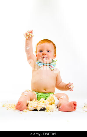 Un bambino arriva a mangiare la torta per la prima volta il suo primo compleanno in questa torta smash in studio contro uno sfondo bianco. Foto Stock