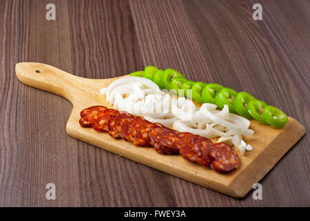 Ungherese piccante, affumicato, salsiccia. Servite su un piatto di legno con un po' di cipolla fresca e pepe verde Foto Stock