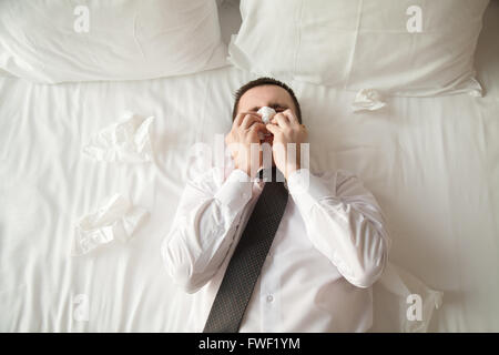 Ritratto di giovane imprenditore che indossa una camicia bianca e cravatta giacente sul letto nella camera di albergo malati con influenza Foto Stock
