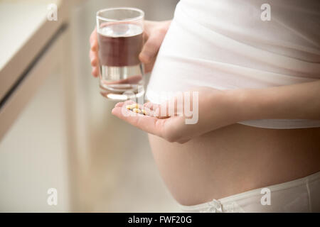 Sanità, trattamento, supplementi. Giovane donna incinta holding giallo compresse rotonde e bicchiere di acqua nella sua mano Foto Stock