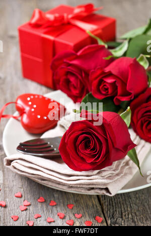 Holiday messa in tavola con rose rosse, confezione regalo su uno sfondo di legno Foto Stock