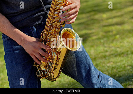 Chiudere fino alle mani di un giovane uomo di suonare il sassofono in un parco Foto Stock