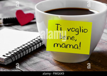La frase ti voglio benne mama, ti amo mamma scritto in italiano in un bigliettino giallo posto in una tazza di caffè, su un woo Foto Stock