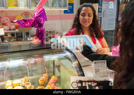 Proprietario attende i clienti utilizzando un iPad dotato di piazza la tecnologia di pagamento a zampillo Splash Sweet Shoppe, la più recente aggiunta ai negozi situati in La Marqueta in East Harlem in New York, visto sul suo giorno di apertura, sabato, 2 aprile 2016. Oltre alla cucina di incubatore nell'edificio ci sono un certo numero di spazi di vendita nel rivitalizzato facility affittati dagli imprenditori e piccole aziende che utilizzano la cucina. (© Richard B. Levine) Foto Stock