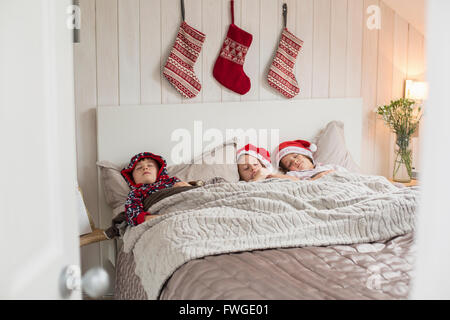 Tre bambini in un letto doppio, con calze di Natale appeso alla parete sopra le loro teste. Foto Stock