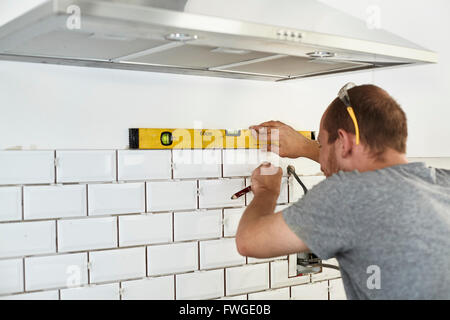 Un uomo che lavora in una cucina nuova, un installatore di piastrelle di applicazione alla parete dietro il fornello. Foto Stock