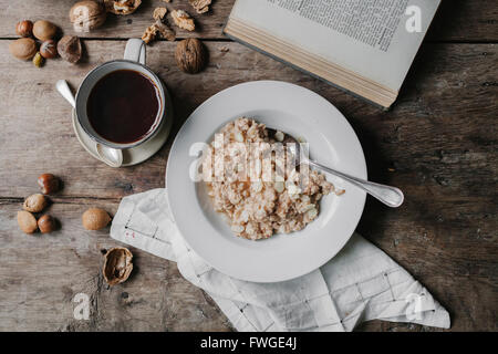 Una tabella con una tazza di caffè, ciotola di muesli, dadi e un libro aperto. Foto Stock