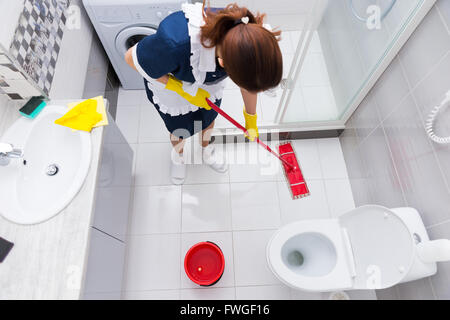 La governante in un hotel con straccio un pavimento in un pulito bagno bianco con un mop, vista da sopra Foto Stock