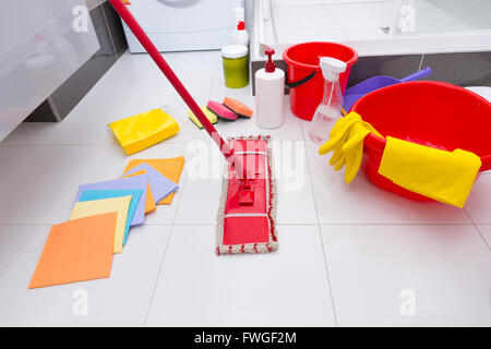 Visualizzazione di un assortimento di prodotti per la pulizia sul pulire il pavimento piastrellato di bianco in un bagno con panni, spugne, mop, benna, bacino e Foto Stock