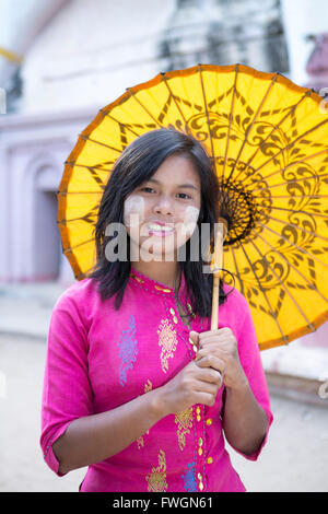 Una ragazza locale con una carta tradizionale ombrellone e faccia thanaka vernice, Monywa, Sagaing, Myanmar (Birmania), Sud-est asiatico Foto Stock