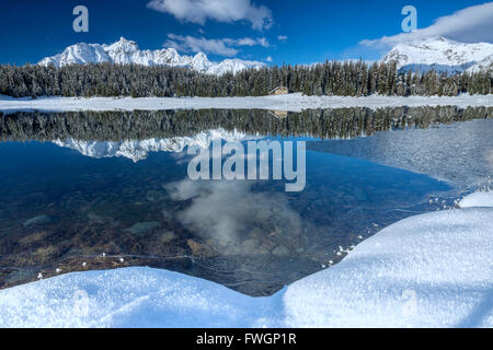 Chalet in legno circondata da vette innevate e boschi si riflette nel Lago Palu, Malenco Valley, Valtellina, Lombardia, Italia, Europa Foto Stock