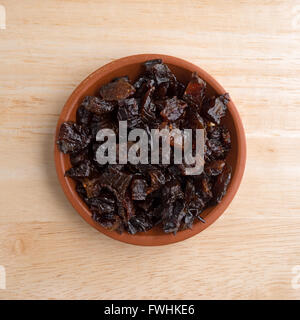 Vista dall'alto di una porzione di prugne a dadini in una piccola ciotola in cima a una tavola di legno alto. Foto Stock