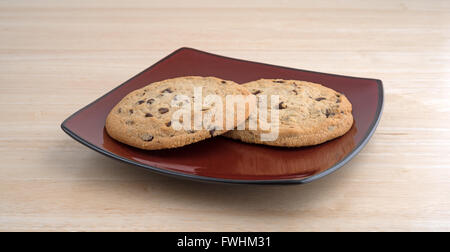 Due chip di cioccolato senza glutine cookies su un profondo targhetta rossa sulla cima di una tavola di legno alto. Foto Stock