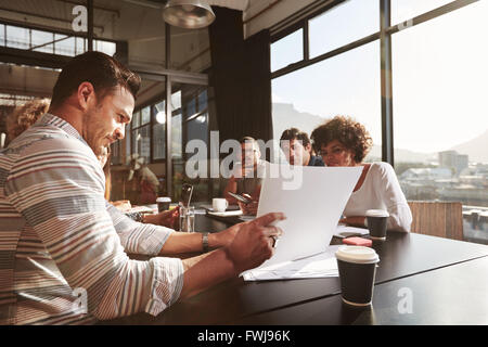 Ritratto di giovane imprenditore spiegando business plan ai suoi colleghi seduti in ufficio. Foto Stock