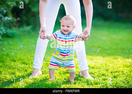 Carino divertente happy baby in un colorato shirt rendendo i suoi primi passi su di un prato verde in un soleggiato giardino estivo Foto Stock