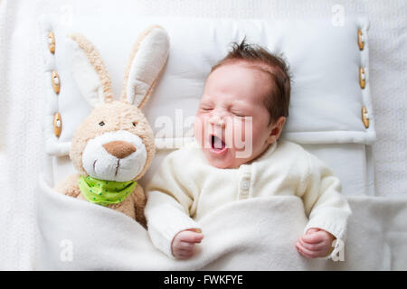 Adorabili sleepy neonato con un giocattolo bunny sbadigli nel letto Foto Stock