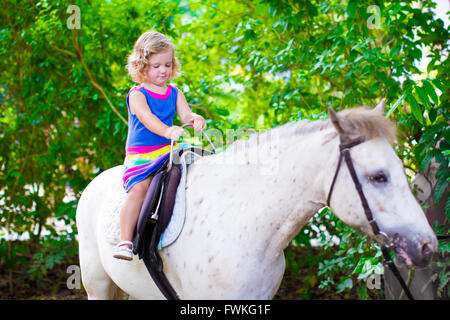 Carino piccolo bimbo ragazza divertirsi su un cavallo godendo di viaggio con la famiglia a uno zoo in una calda giornata estiva Foto Stock