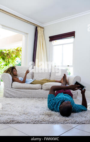 Donna di guardare la televisione mentre uomo disteso sul tappeto Foto Stock