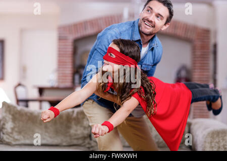 Padre e figlia fingendo di essere il supereroe in salotto Foto Stock