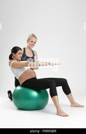 Donna incinta facendo esercizio di fitness con personal trainer Foto Stock