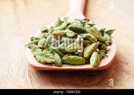 Green i semi di cardamomo mucchio sul cucchiaio di legno rustico sfondo tabella Foto Stock