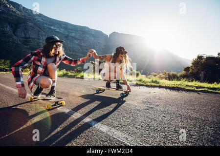 Felice coppia giovane divertirsi con lo skateboard su strada. Giovane uomo e donna pattinaggio insieme in una giornata di sole. Foto Stock