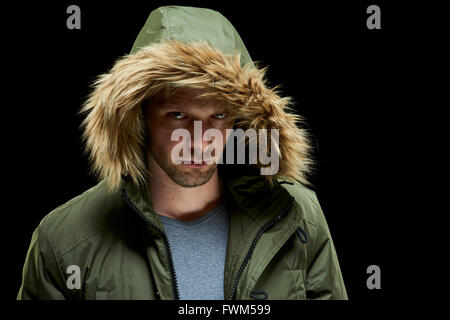 Tasto basso ritratto in studio dei casi sospetti giovane adulto modello caucasico indossando cappotto invernale con cappa a. Foto Stock