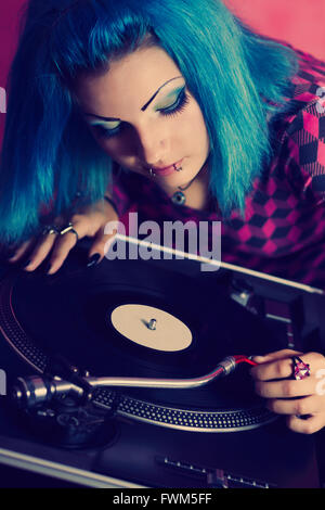 Elegante ragazza giovane DJ con tinti di blu capelli mettere un ago su un record con la musica. Piattaforma girevole professionale attrezzature per un DJ, nightclub e appassionati di audio Foto Stock