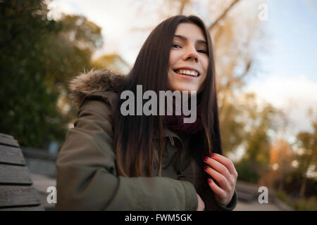 Sorridente tanga giovane ragazza nel parco grigio cappotto e sciarpa di marsala. Modello di divertenti con pug naso e amichevole o felice espressione facciale Foto Stock