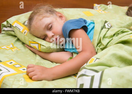 Bambina che dorme sul suo lato nel letto con la mano sotto il cuscino e coperta con una coperta Foto Stock