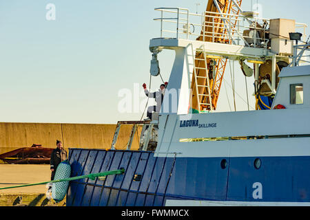 Simrishamn, Svezia - Aprile 1, 2016: due persone di lavorare sul fianco di una barca da pesca, ottenendo una fune su un cilindro. Uno di essi è Foto Stock