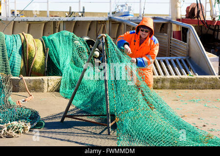 Simrishamn, Svezia - Aprile 1, 2016: pescatore permanente sulla dockside rammendo il suo verde le reti da pesca. Persone reali nella vita di tutti i giorni. Foto Stock