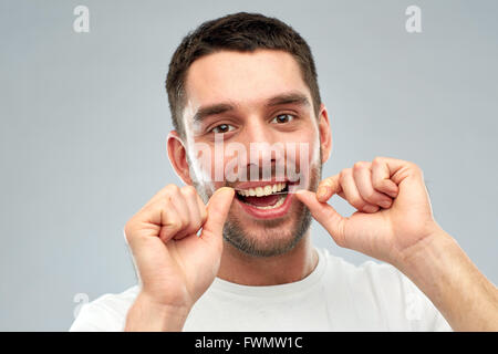 Uomo con filo interdentale pulizia di denti su grigio Foto Stock