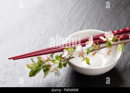 I sushi giapponesi Le bacchette, la salsa di soia ciotola e sakura blossom sulla pietra nera dello sfondo. Vista da sopra con lo spazio di copia Foto Stock