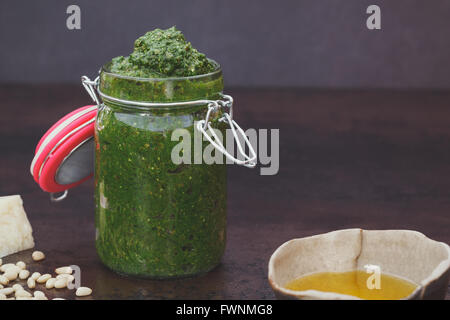 In casa il pesto. In casa il pesto in un vasetto e gli ingredienti su sfondo scuro. Macro, il fuoco selettivo, vintage tonico, immagine vuota Foto Stock